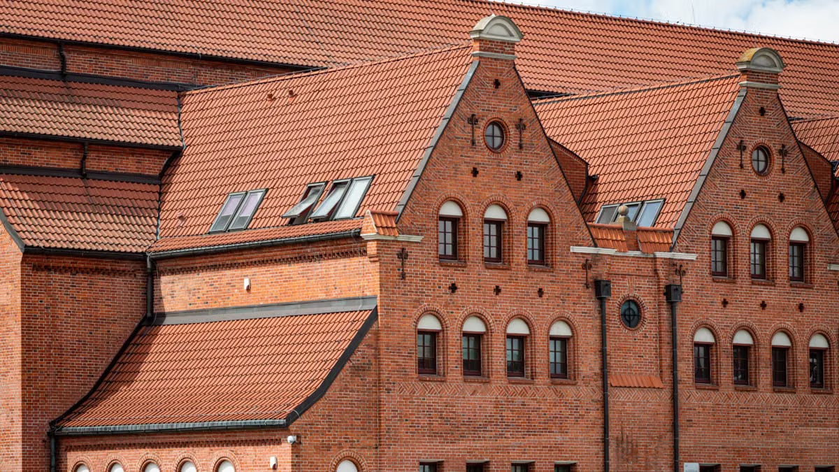 Red brick facade of a historic building in Gdańsk, Poland with intricate roof design.