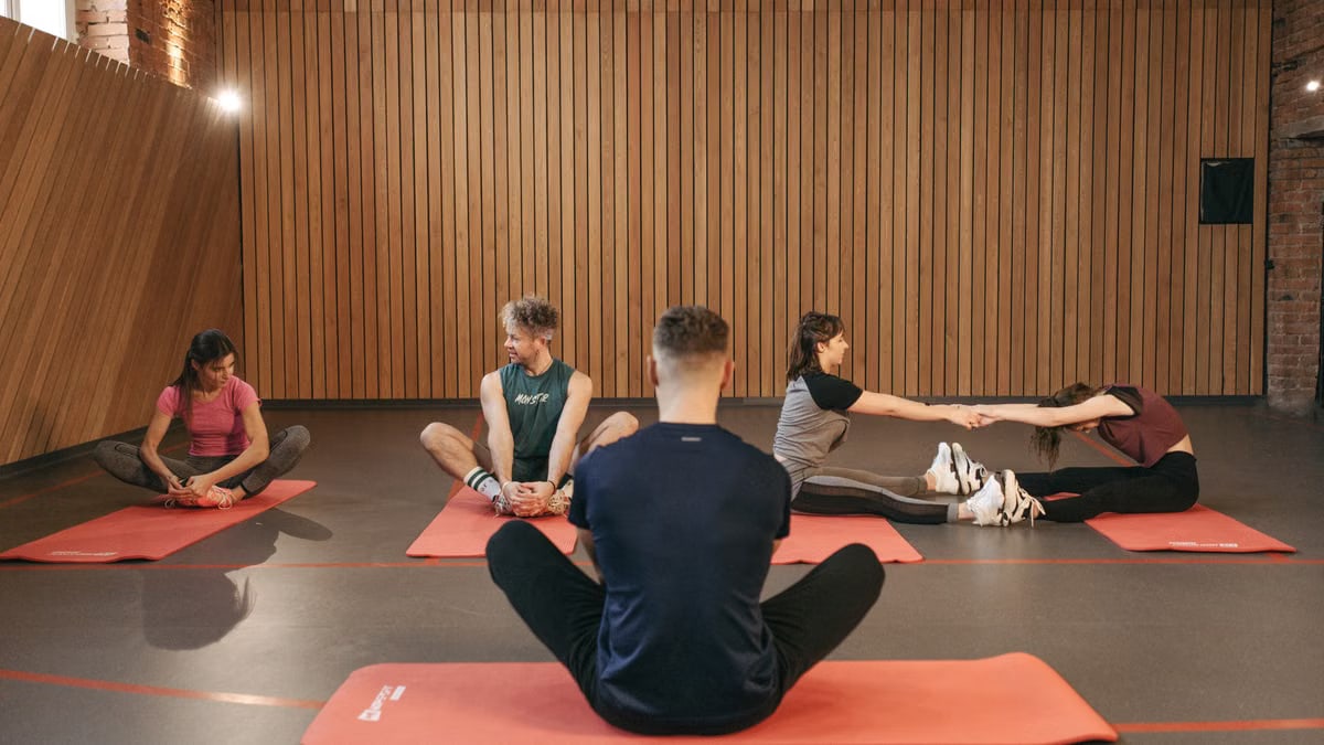 A group of adults practicing yoga and stretching on mats in a wooden panelled room.